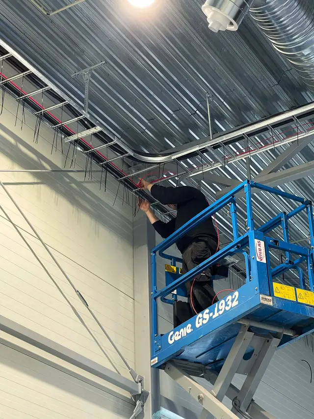 Montør på saksløfter trekker kabler i taket i et nybygg
