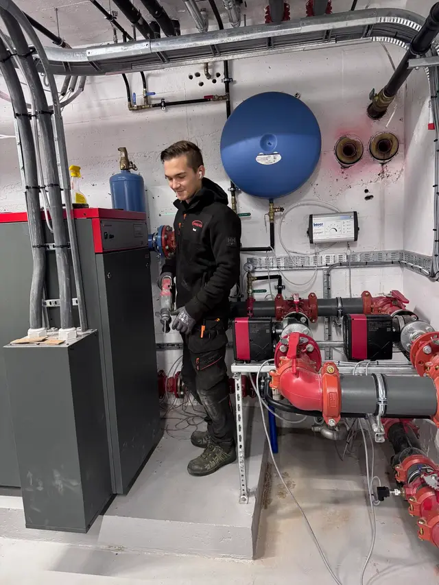 Montør i et teknisk rom med rør og pumper