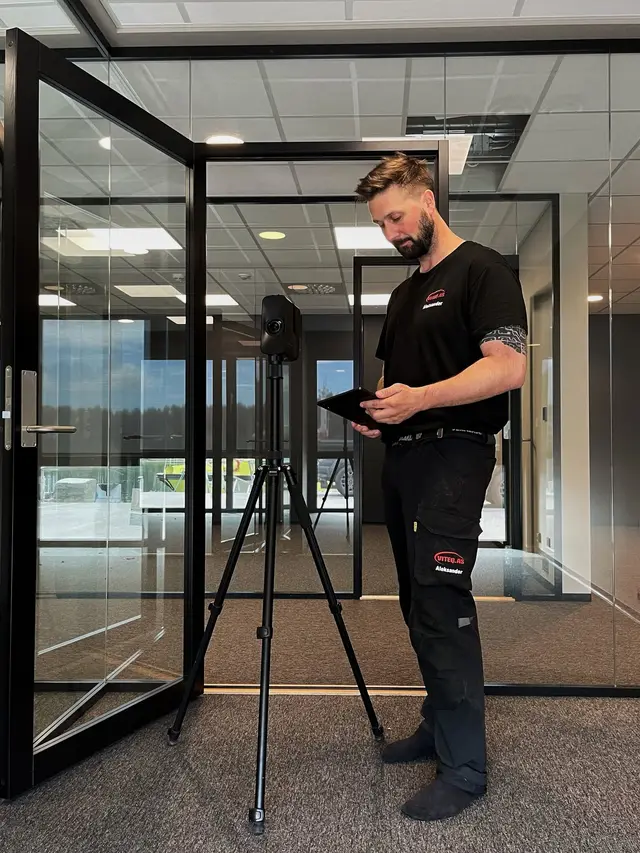 Ansatt med nettbrett ved en laserskanner på stativ